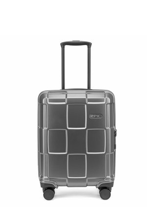 Valise rigide grise avec poignée télescopique étendue, quatre roues multidirectionnelles et motif carré texturé sur la face avant.