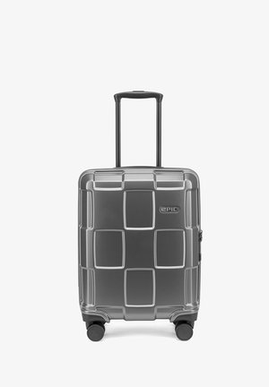 Valise rigide grise avec poignée télescopique étendue, quatre roues multidirectionnelles et motif carré texturé sur la face avant.