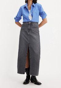 Šedá denimová maxi sukně s předním rozparkem, doplněná modrou košilí na knoflíky a černými kotníkovými botami. Sukně má vysoký pas a strukturovaný střih.