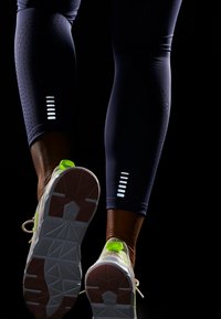 Navy leggings feature perforated texture and reflective accents. White athletic shoes have a green heel tab and a textured white and pink sole.
