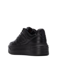 Zapatillas negras con parte superior de cuero texturizado, suela de plataforma, cuello acolchado y costuras tonales. Presenta un logo embosado en el talón.