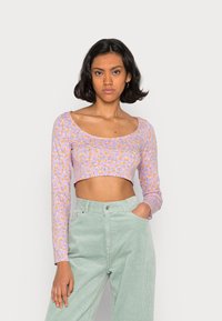 Top cropped de manga longa em lilás com um padrão floral. Combinado com calças de veludo cotelê de cintura alta em verde claro. Textura suave e design justo.