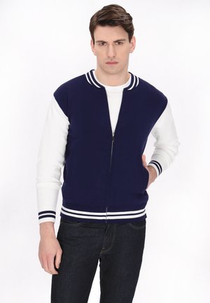 Zip-up jakke med en navy krop, hvide ærmer og stribede ribkanter. Den har en afslappet pasform og to frontlommer.