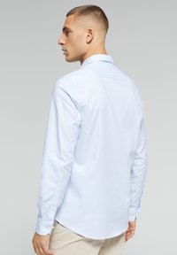 Lichtblauw langemouwen shirt met een puntige kraag, gladde textuur en knoopmanchetten. Heeft een gebogen zoom en minimale details.
