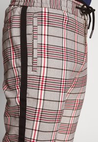 Rutiga byxor i grått med röda och svarta ränder. Har resår i midjan och sidoficka. Materialet verkar ha en texturerad och vävd yta.