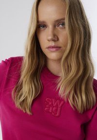 Roze trui met een gestructureerd "swag" logo, voorzien van een geribde halslijn en korte mouwen. Glad materiaal en casual pasvorm.