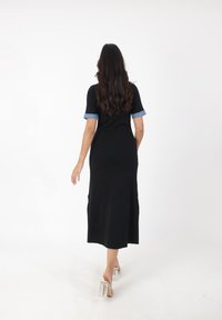 Zwart geribbelde gebreide jurk met korte, denimaccenten mouwen, die tot halverwege de kuit reikt; model draagt doorzichtige hakken.