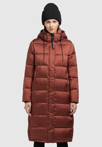 Long, padded coat in rust-colored synthetic fabric with a high collar, drawstring hood, and vertical quilting. Features side pockets.