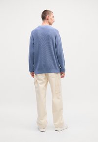 Suéter de malha texturizada azul com um corte solto, combinado com calças cargo bege com bolsos laterais e uma perna ligeiramente afunilada.