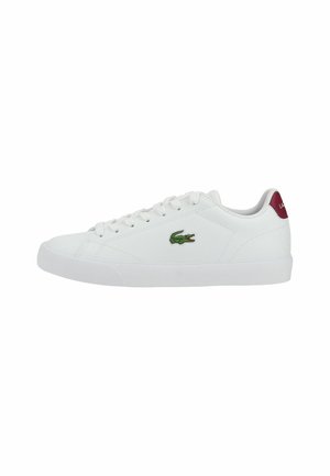 Witte lage sneaker met witte veters, groen krokodillenlogo aan de zijkant en rode hieltab met witte tekst.