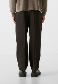 Pantalones de pierna ancha negros con una textura suave, cintura alta y detalles en las costuras laterales. Combinados con una parte superior texturizada de color claro y zapatos negros gruesos.