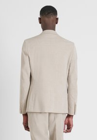 Blazer di lino beige con spalle strutturate, apertura singola, polsini con bottone e una superficie liscia, visto da dietro.