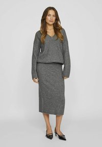 Suéter de punto gris con textura acanalada y escote en V, combinado con una falda larga a juego. Zapatos de tacón negro con punta afilada completan el conjunto.