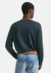 Pull en gris foncé à manches longues avec un col rond. Porté avec un jean en denim bleu clair et une ceinture en cuir tressé marron. Design simple et décontracté.