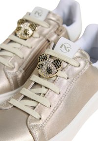 Sneakers metallici oro con lacci crema. Presentano un'ornamentazione a testa di panda gioiello sui lacci e una fodera interna bianca.