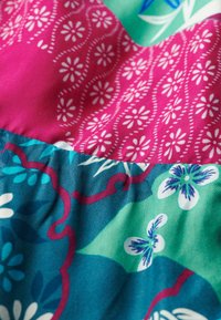 Tela colorida con patrones florales y geométricos en rosa, verde azulado y verde, con una textura suave y acentos blancos contrastantes.