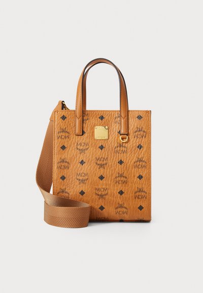 Tan leather handbag with black logo pattern, square shape, top handles, and a detachable textured strap. Gold hardware detail present.