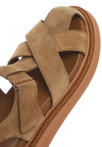 Brown suede sandal with crossed straps, thick tan sole featuring a braided texture, and a smooth inner footbed.