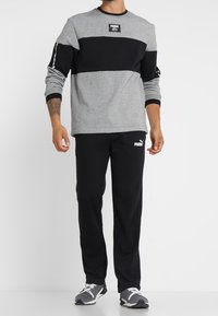 Grå och svart atletisk sweatshirt med långa ärmar, ribbad krage och logotyp patch; parat med svarta sweatpants med logotypdetaljer.