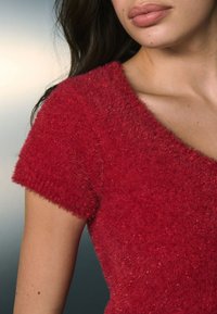Crveni majica od mekanog materijala s kratkim rukavima, karakterizirana mekim teksturom i širokim izrezom. Istaknuta suptilnim sjajem u tkanini.