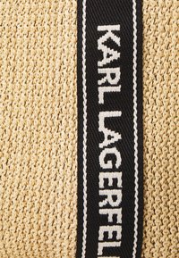 Geflochtene Strohtasche mit einer strukturierten beige Oberfläche und einem schwarzen Stoffriemen, auf dem "KARL LAGERFELD" in weißer Schrift angezeigt wird.