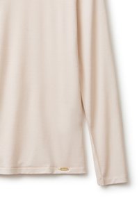 Camicia beige chiaro a maniche lunghe con tessuto morbido e piccolo logo rettangolare dorato vicino all'orlo su sfondo bianco.