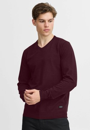 Maroon long-sleeve v-neck sweater with a smooth texture, fitted design, and a small black brand tag on the lower side.