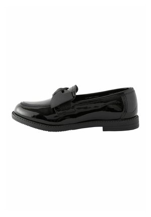 Mocasín de charol negro con puntera redondeada y gran lazo de tela encima, suela plana de goma, vista lateral.