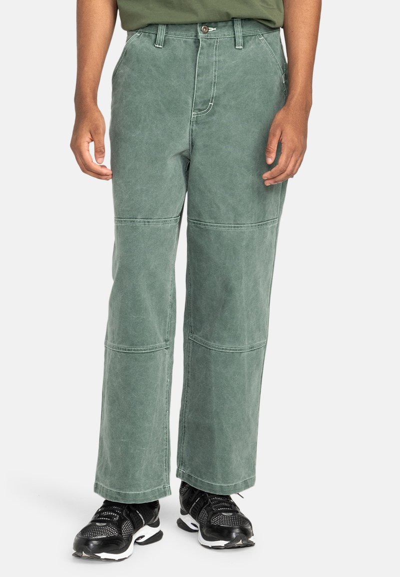 Green, wide-leg pants made from cotton, featuring patchwork design and visible seams. Paired with black sneakers.