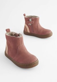 Botine din suede roz cu căptușeală din blană sintetică, fermoar lateral și tălpi din cauciuc maro texturat. Prezintă dungi laterale în nuanțe mai deschise.
