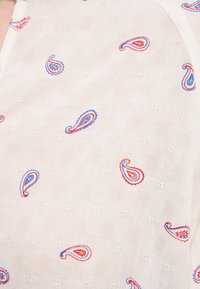 Tessuto bianco con un motivo a quadretti testurizzato. Motivi paisley rossi e blu sparsi su tutta la superficie. Aspetto leggero e arioso.