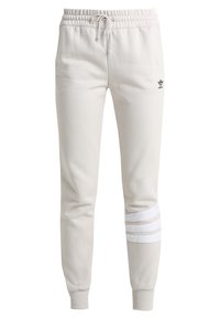 Ljust beige sweatpants med elastiskt midjeband, dragsnören och tre vita horisontella ränder på vänster ben. Svart logotyp på höger höft.