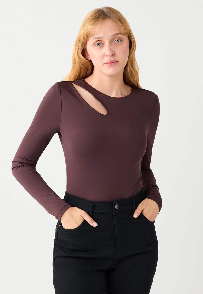 Haut marron à manches longues avec un col rond et un détail d'ouverture latérale. Associé à un pantalon noir taille haute. Texture de tissu lisse.