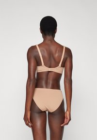 Nude two-piece swimwear set featuring a textured bralette with adjustable straps and matching high-waisted bikini bottom. Smooth, fitted texture.