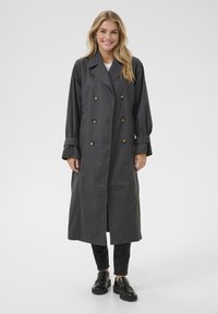 Trench coat lungo di un grigio scuro, con design doppiopetto, caratterizzato da bottoni dorati, vestibilità rilassata e polsini arrotolati. Abbinarlo a pantaloni neri e scarpe.