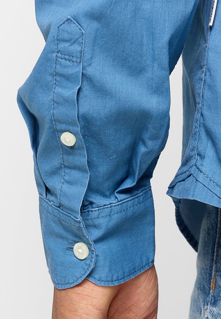 Hellblaues, langärmeliges Hemd mit Knöpfen, featuring weiße Knöpfe, weichem Material und genähten Details an den Bündchen.