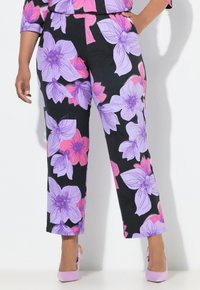 Schwarze Hose mit lebhaftem lila und pinkem Blumenmuster, geradem Bein und Taschen. Kombiniert mit hellrosa Absätzen.