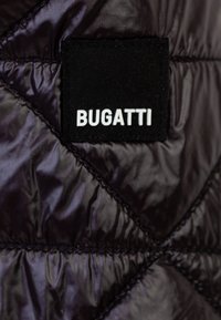 Tessuto trapuntato nero con una texture lucida, caratterizzato da un'etichetta rettangolare nera con il testo bianco "BUGATTI" in un carattere audace.