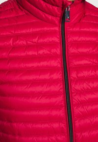 Červená prošívaná péřovka s vysokým límcem, vybavená černým zipem po celé délce a horizontálním prošíváním pro izolaci. Hladký, lesklý textilní povrch.