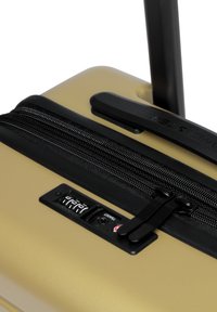 Valigia rigida di colore oro metallico con zip nera, lucchetto a combinazione e manico telescopico per una facile mobilità.