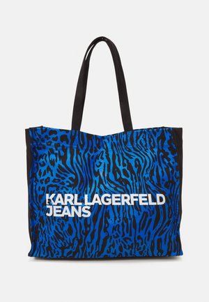 Sac fourre-tout bleu et noir présentant un motif à rayures zébrées, fabriqué en tissu avec des poignées noires solides. Le texte indique "KARL LAGERFELD JEANS."