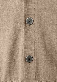 Beżowa dzianina z dwoma szarymi guzikami z czterema otworami, każdy przyszyty i umieszczony na środku dziurek na guziki wzdłuż pionowego zakładki.