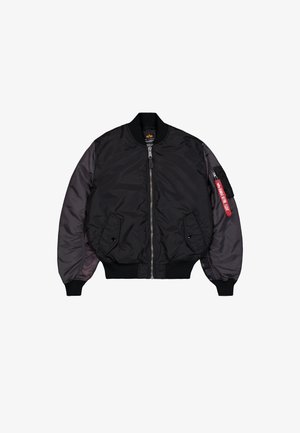 Black bomber jacket with front zipper, ribbed cuffs, two flap pockets, and a zippered arm pocket featuring a red "Remove Before Flight" tag.