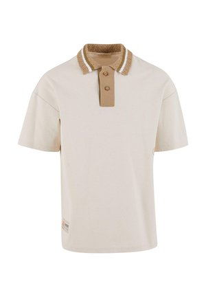 Lyhythihainen polo-paita vaaleanbeigessä värissä, jossa on samalla tekstuurilla varustettu ruskea kaulus, kahdella napilla ja valkoisilla korostusraidoilla kauluksessa.