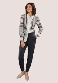 Langemouwen shirt met een geometrisch patroon in zwart en wit, gecombineerd met slim-fit zwarte broek en lichtgrijze puntige ballerina's.