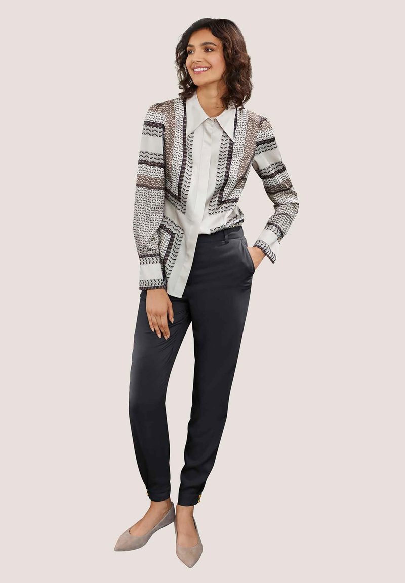 Langemouwen shirt met een geometrisch patroon in zwart en wit, gecombineerd met slim-fit zwarte broek en lichtgrijze puntige ballerina's.