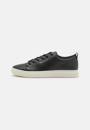 Shoe de couro preto com bico redondo, sola de borracha branca em contraste, fecho de atacadores com seis furos e uma marcação discreta na lateral.