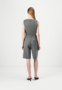 Gray tailored jumpsuit with sleeveless design, belted waist, and knee-length shorts. Smooth texture with functional back pockets.