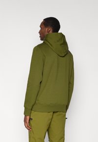 Φούτερ σε ελιά πράσινο με κουκούλα με κορδόνι, μαλακό βαμβακερό ύφασμα, ριμπ μανσέτες και λογότυπο κοντά στον λαιμό, σετ με ταιριαστό παντελόνι.