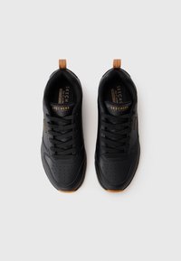 Black athletic shoes with a smooth leather upper, perforated design, flat laces, and a brown heel tab. Features a rubber outsole.